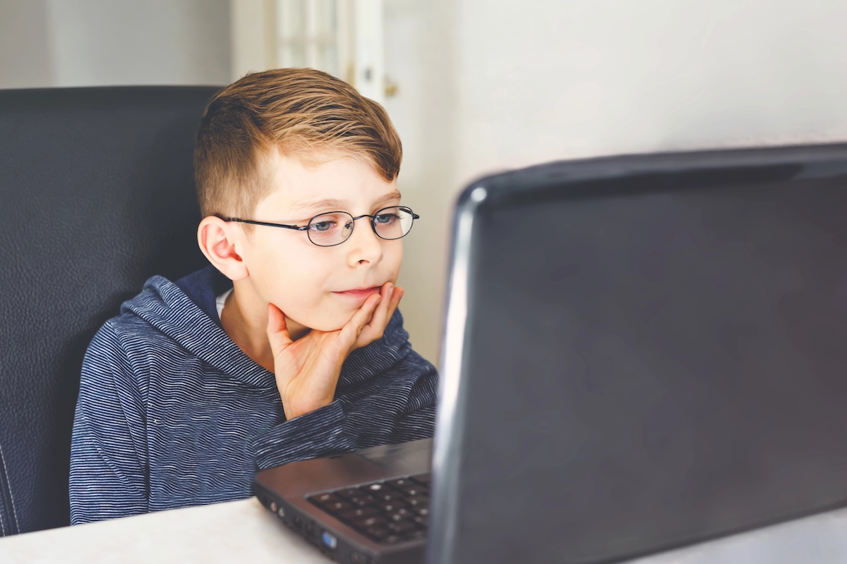 Niño usando lentes mientras ve algo en una laptop, representando la miopía en niños y tratamientos para controlarla.